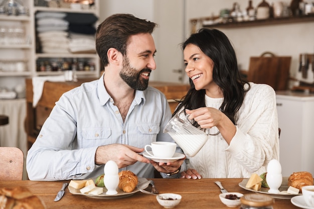 Portrait of cheery european couple man and woman drinking coffee while having breakfast in kitchen at home