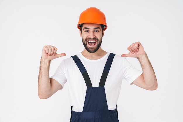 Portrait of a cheery optimistic young man builder in helmet posing isolated over white wall pointing to himself.