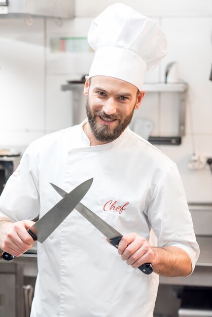 Portrait of chef cook in uniform with knifes at the restaurant kitchen