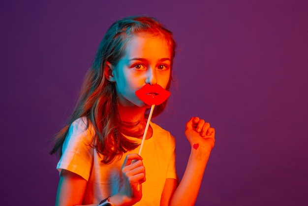 Portrait of a child girl The girl put paper lips to her lips on a purple background