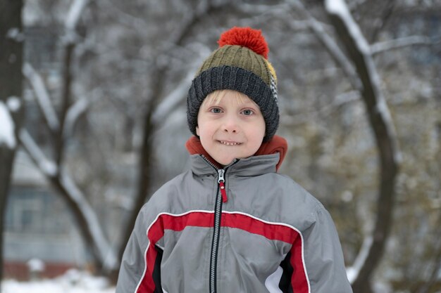 Photo portrait of child in winter hat against snowy yard background.