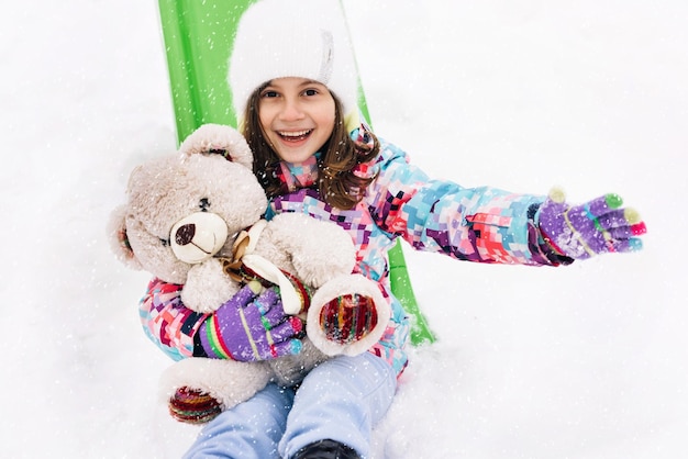 Portrait of child with toy teddy bear sits on a sled and looks at the winter snowy mountainswinter