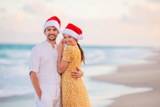 Portrait of Christmas happy couple in Santa hats on beach vacation having fun