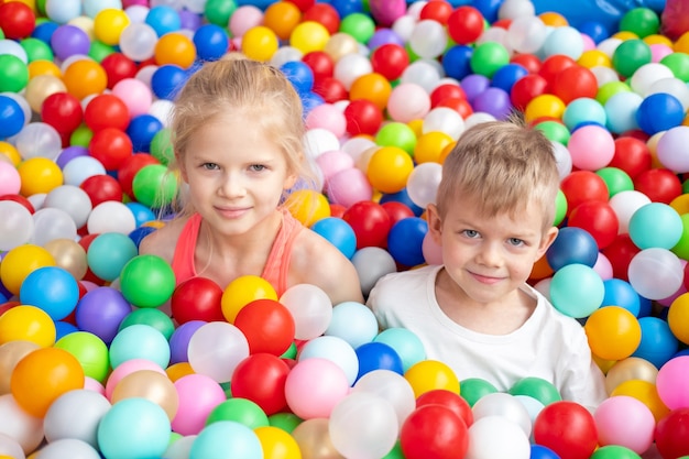 Portrait close up smiling blonde little boy and girl lying on multi colored plastic balls in big dry