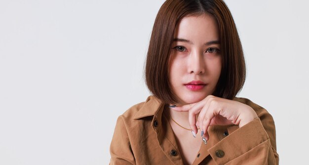 Portrait close up studio cutout shot of Asian stressed depressed worried thoughtful moody short hair female model in long sleeve brown shirt holding hand on forehead have headache on white background.