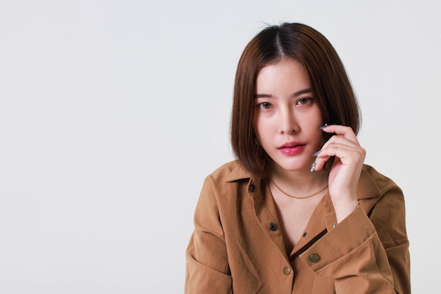 Portrait close up studio cutout shot of Asian stressed depressed worried thoughtful moody short hair female model in long sleeve brown shirt holding hand on forehead have headache on white background.