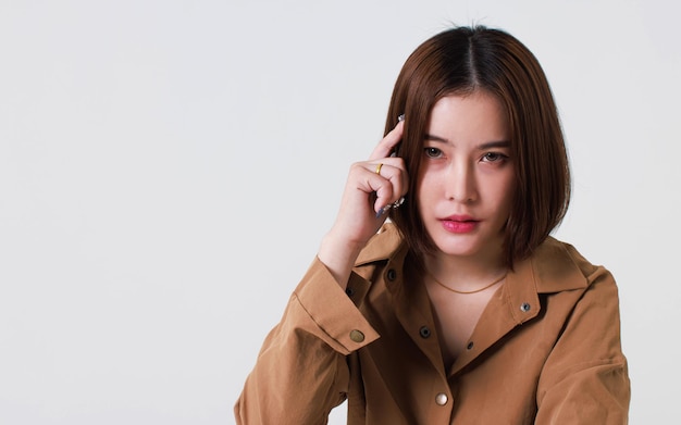 Portrait close up studio cutout shot of Asian stressed depressed worried thoughtful moody short hair female model in long sleeve brown shirt holding hand on forehead have headache on white background.