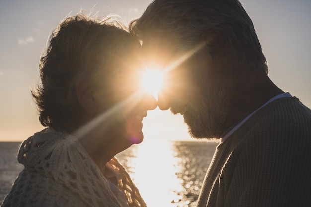 Portrait and close up of two happy in love seniors looking to each other smiling with the sun of the sunset between their heads