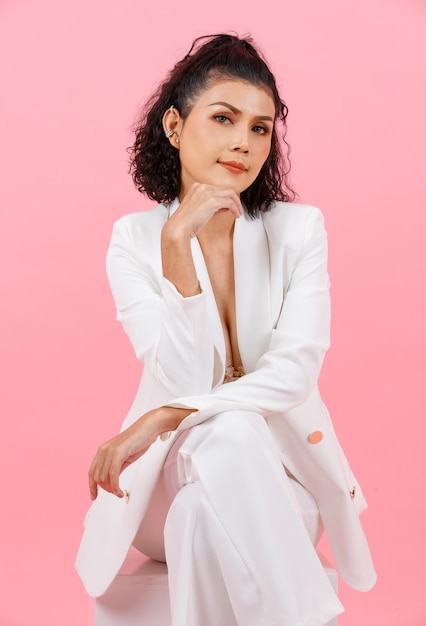 Portrait closeup studio shot Asian young sexy curly hairstyle professional successful businesswoman in white fashion casual suit and lace bra sitting smiling crossed legs posing on pink background