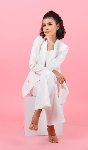 Portrait closeup studio shot Asian young sexy curly hairstyle professional successful businesswoman in white fashion casual suit and lace bra sitting smiling crossed legs posing on pink background