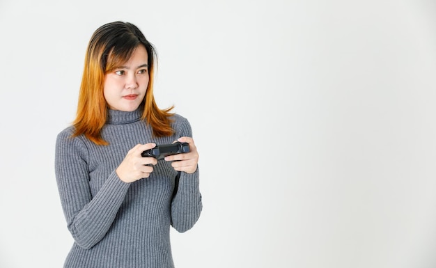 Portrait closeup studio shot of Asian young teen female model gamer in gray turtleneck dress standing smiling holding 3d video game dualshock console joystick in hands playing on white background.