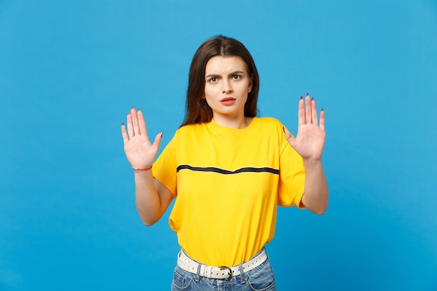 Portrait of concerned young woman in vivid casual clothes looking camera, rising hands, showing palms isolated on bright blue background wall in studio. People lifestyle concept. Mock up copy space.