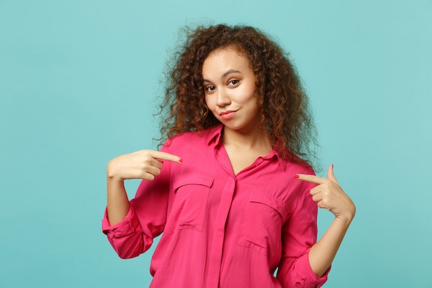 Portrait of confident african girl in casual clothes pointing index fingers on herself isolated on blue turquoise background in studio. People sincere emotions, lifestyle concept. Mock up copy space.