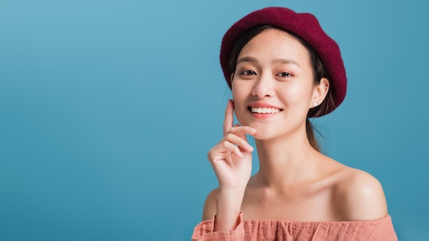 Portrait of confident beautiful asian woman with hand beside face and looking to camera isolated on blue color background with studio shotSkincare for healthy face concept