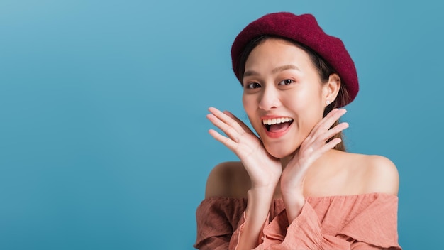 Portrait of confident beautiful asian woman with hand beside face and looking to camera isolated on blue color background with studio shotSkincare for healthy face concept