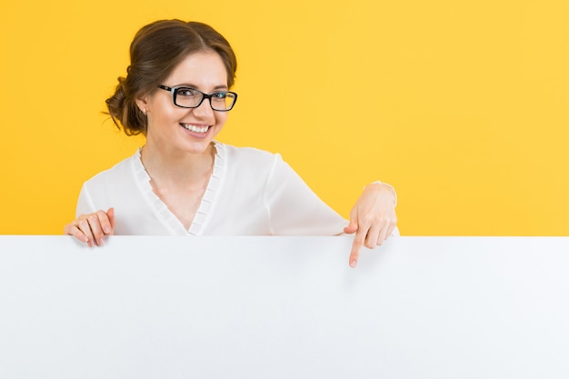 Portrait of confident beautiful young business woman showing blank billboard on yellow background