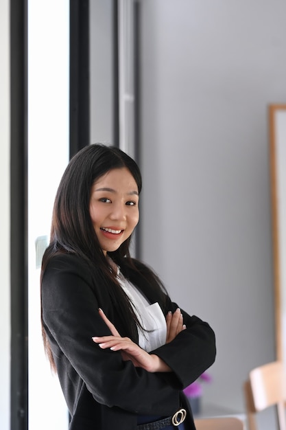 Portrait of confident businesswoman in suit standing with crossed near office window