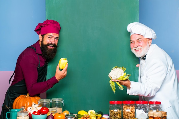 Portrait of a confident chef showing vegetables and fruits on copyspace blackboard two chief cook se...