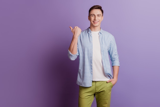 Portrait of confident guy toothy smile direct thumb empty space on purple background