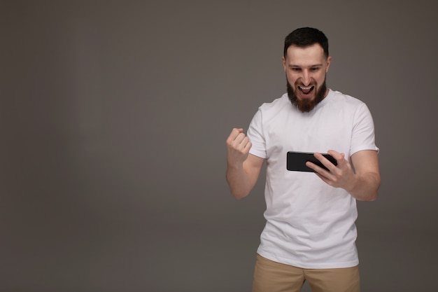 Portrait of a confident happy man holding mobile phone and celebrating success isolated over grey background