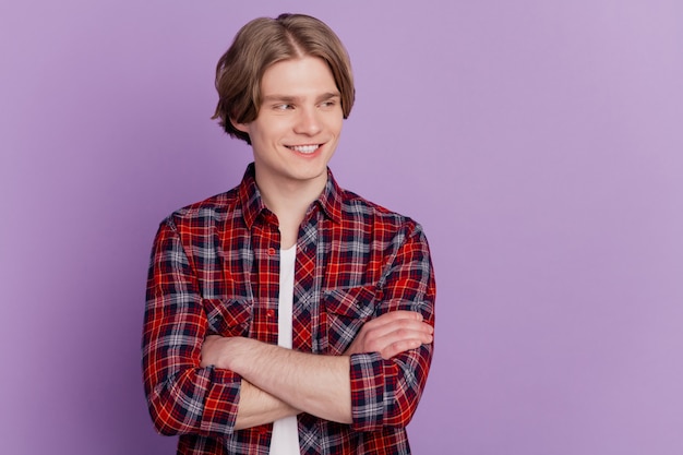 Portrait of confident interested guy crossed arms look empty space on purple background