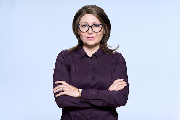 Portrait of confident mature woman in glasses looking at camera on light background