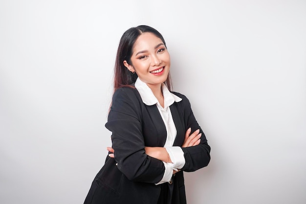 Portrait of a confident smiling Asian girl boss wearing black suit standing with arms folded and looking at the camera isolated over white background