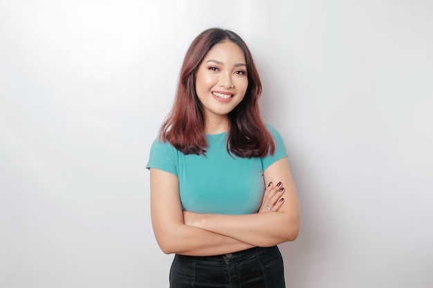 Portrait of a confident smiling Asian woman wearing blue shirt standing with arms folded and looking at the camera isolated over white background