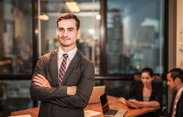 Portrait of confident smiling businessman standing against colleagues in board room