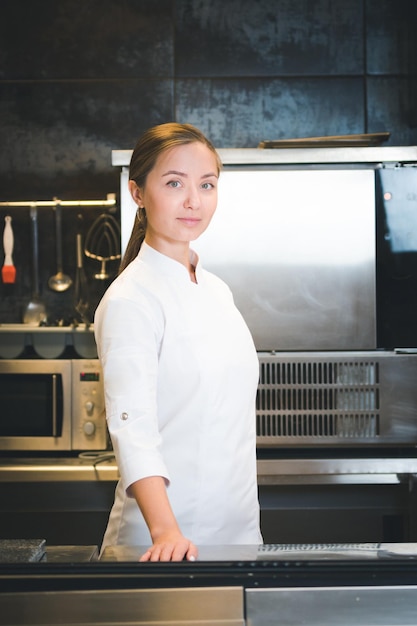 Portrait of confident and smiling young woman chef dressed in white uniform professional kitchen are on background