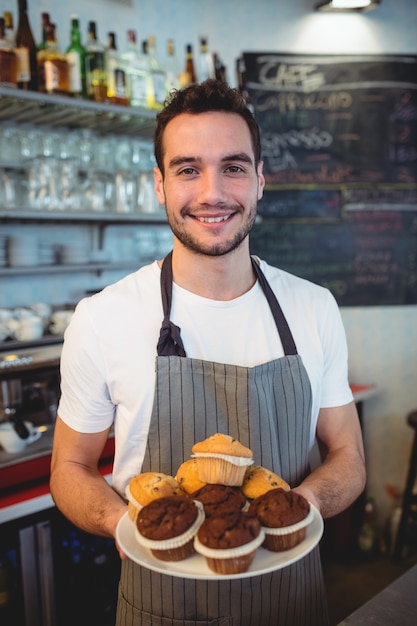 Portrait of confident waiter with cupcakes at cafe