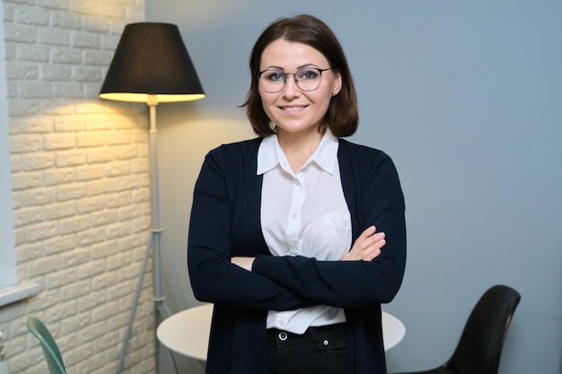 Portrait of confident woman psychologist, psychotherapist, social worker, teacher with folded arms, looking at camera in office