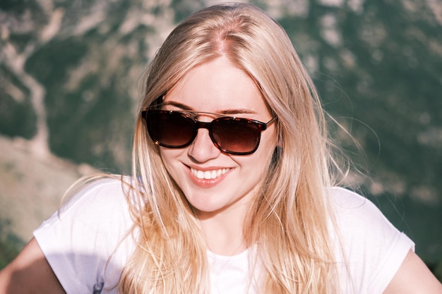 Portrait confident young cheerful smiling blonde woman looks into the camera wearing sunglasses agai