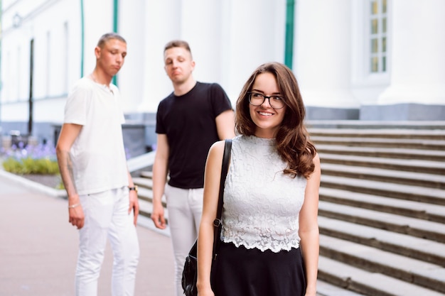 Portrait of confident young woman. Two guys behind her with evaluation look.