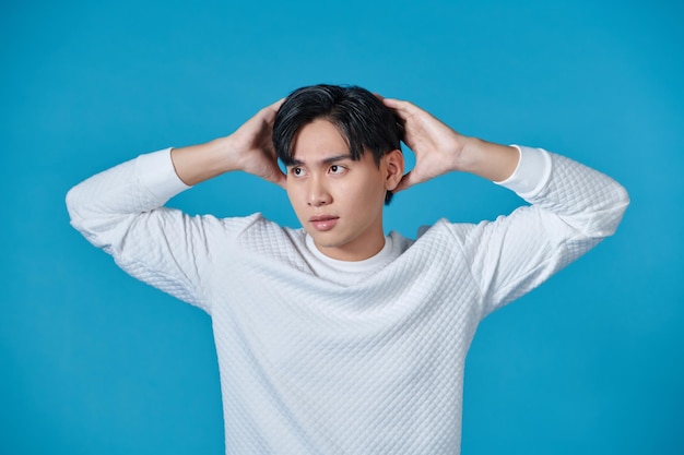 Portrait of a confused asian man holding hands on his head isolated over blue background