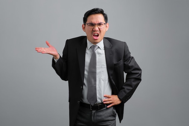 Portrait of confused handsome young businessman in formal suit shrugging hands sideways and looking disappointed isolated on grey background