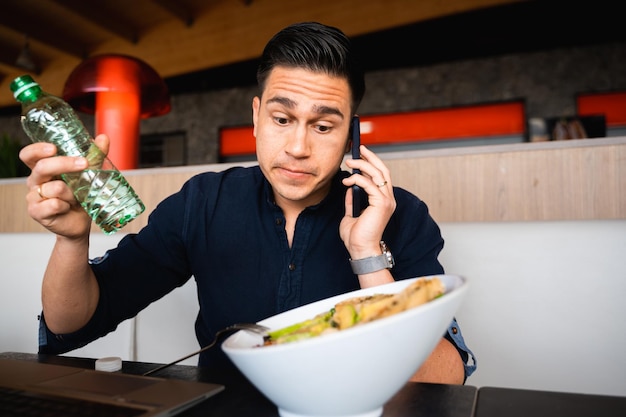 Portrait confused uncertain male talking at phone sitting at table have healthy lunch with salad