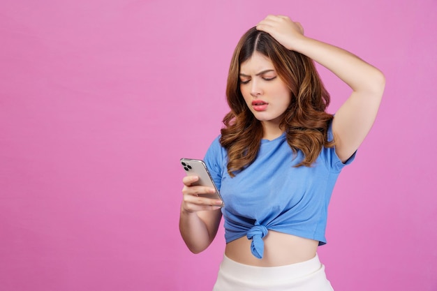 Portrait of confused young woman wearing casual tshirt using smartphone isolated over pink background