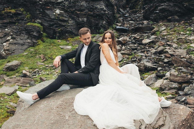 Portrait of a couple taking a photo shoot on their wedding day sitting on a stone back to back on th