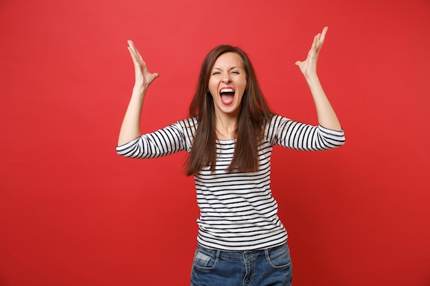 Portrait of crazy young woman in casual striped clothes screaming, rising and spreading hands 