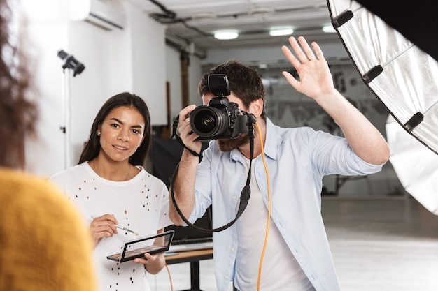 Portrait of creative photographer man shooting beautiful female model with professional camera and softbox in studio