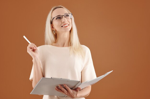 Portrait of creative smiling businesswoman in glasses writing down her ideas in document and looking up