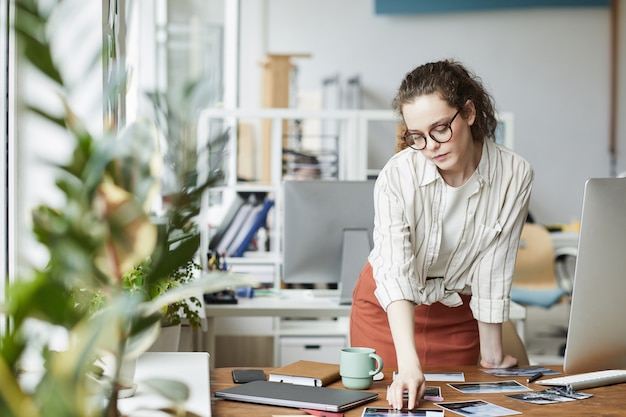 Portrait of creative young woman reviewing photographs while working on editing and publishing in modern office, copy space