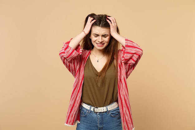 Portrait of crying displeased young woman in casual clothes putting hands on head isolated on pastel beige wall background in studio. People sincere emotions, lifestyle concept. Mock up copy space.