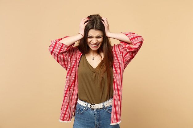 Portrait of crying frustrated young woman in casual clothes putting hands on head isolated on pastel beige wall background in studio. People sincere emotions, lifestyle concept. Mock up copy space.