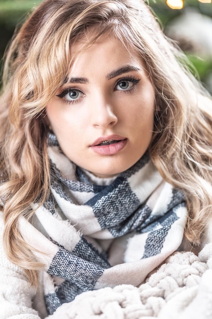 Portrait of a curly blonde woman with knitted sweater and checkered scarf in front of a christmas tree