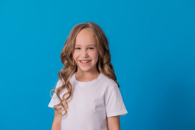 portrait of a curly-haired girl in jeans and a white T-shirt on a blue background