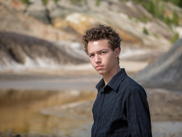 Portrait of a curly-haired teenage boy on the background of a mountain landscape