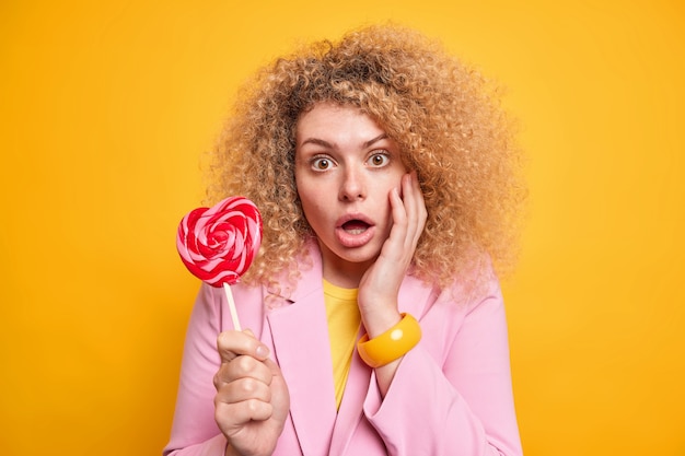 Portrait of curly haired woman looks amazed at camera