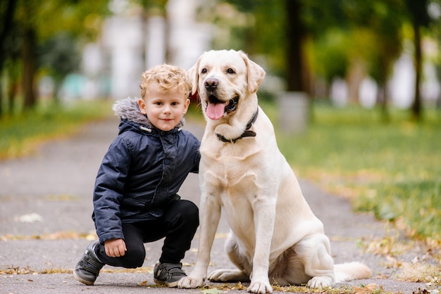 Portrait of cute adorable little Caucasian baby boy sitting with dog in park outside. Smiling child holding animal domestic pet. Happy childhood concept